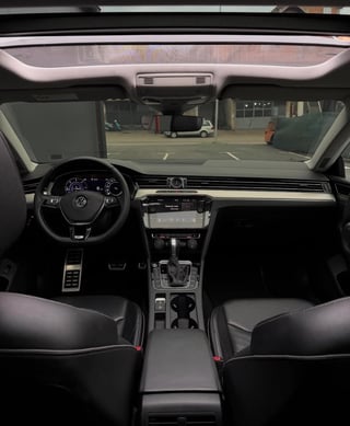 Interior view of a Volkswagen car showing dashboard, steering wheel, and windshield view of parking garage