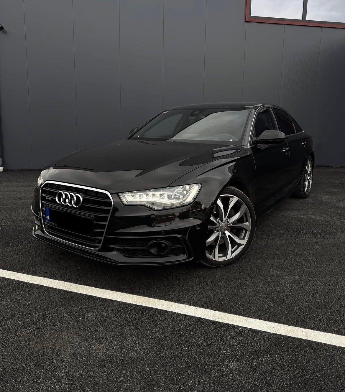 Black Audi sedan parked in indoor garage with gray walls and white parking line