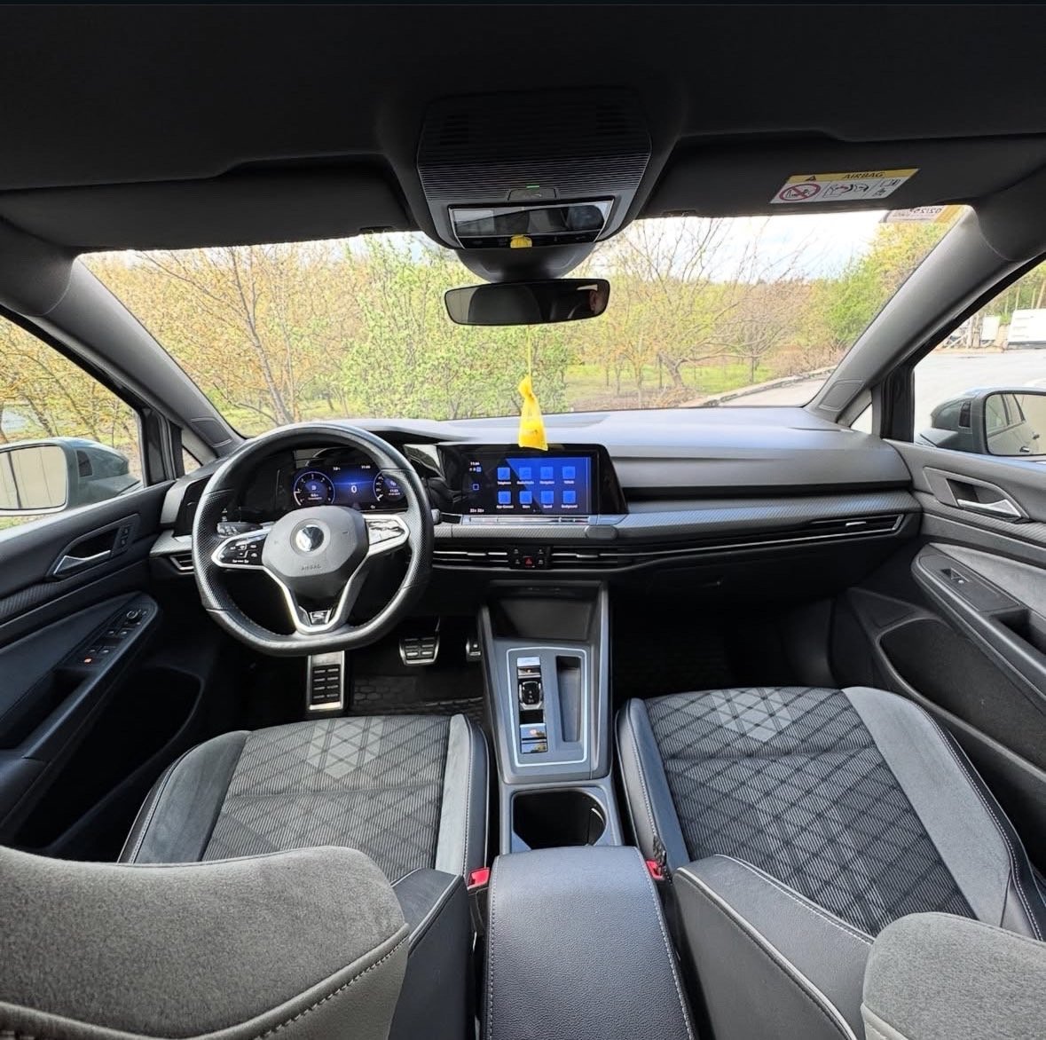 Interior view of a modern car showing steering wheel, digital dashboard with blue display, and gray quilted seats with panoramic sunroof