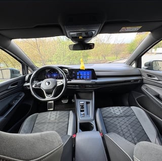 Interior view of a modern car showing steering wheel, digital dashboard with blue display, and gray quilted seats with panoramic sunroof