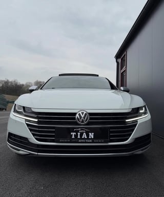 White Volkswagen Arteon sedan parked in front of a dark building, front view showing LED headlights and grille