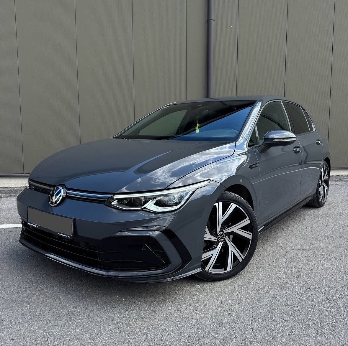 Blue Volkswagen Golf ID electric car parked in front of gray ribbed wall, angled front-left view