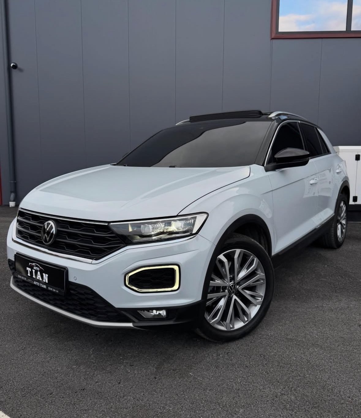 White Volkswagen T-ROC SUV parked in front of a gray metal building