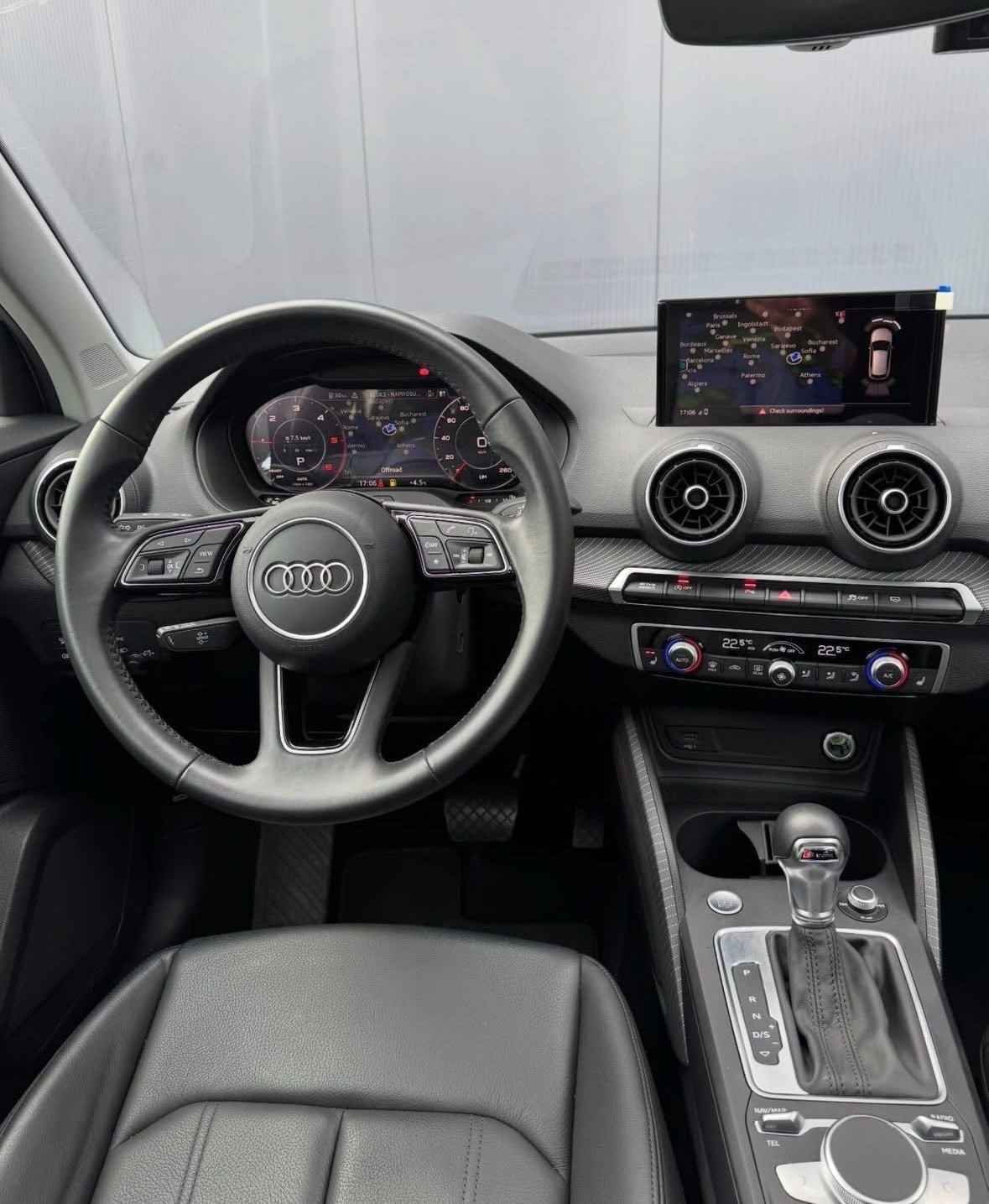 Interior of Audi vehicle showing steering wheel, digital dashboard, touchscreen display, and black leather seats