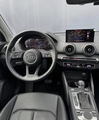 Interior of Audi vehicle showing steering wheel, digital dashboard, touchscreen display, and black leather seats