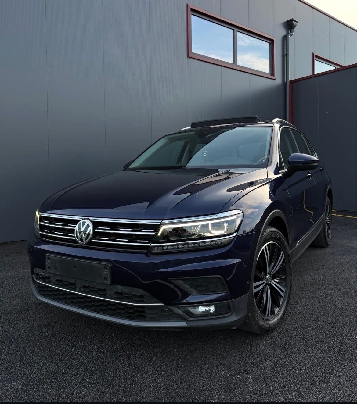 Dark blue Volkswagen SUV parked against a gray metal building with windows