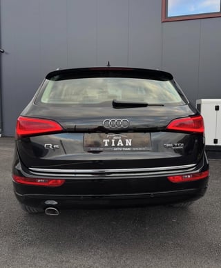 Black Audi Q5 SUV photographed from the rear, showing red taillights and license plate, parked in front of a gray building