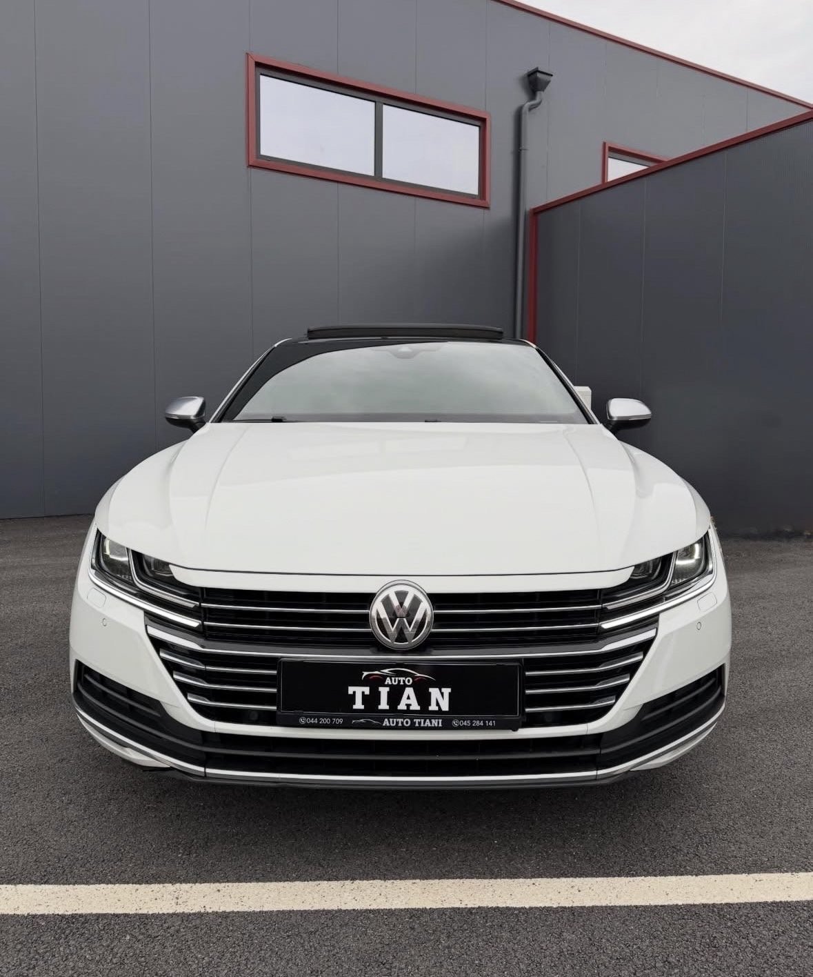 White Volkswagen sedan parked in front of gray industrial building with red metal framing and window