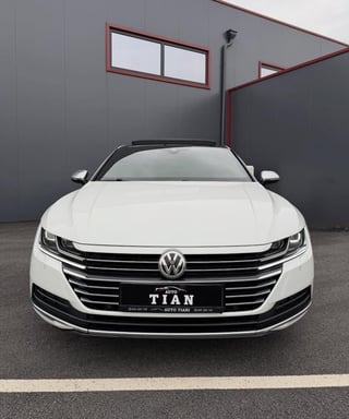 White Volkswagen sedan parked in front of gray industrial building with red metal framing and window