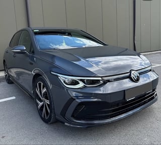 Black Volkswagen Golf electric vehicle parked in front of gray corrugated metal wall