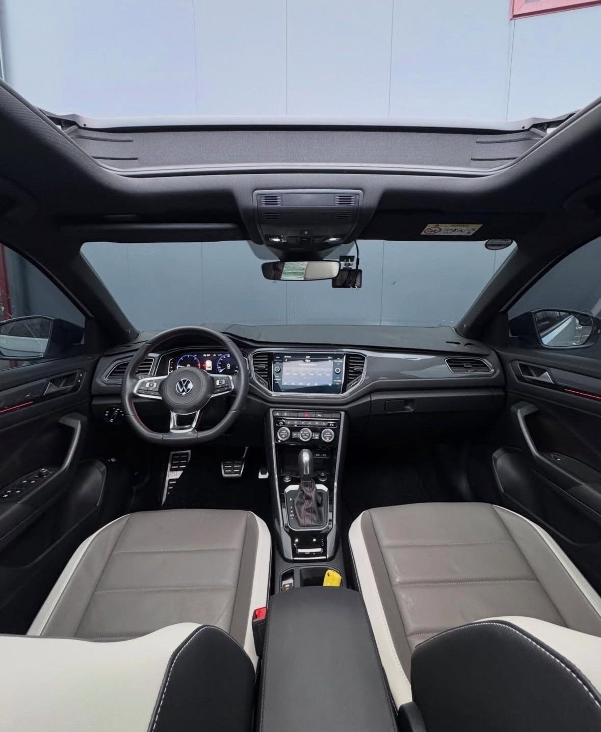 Interior view of a modern Volkswagen vehicle showing steering wheel, dashboard with touchscreen display, dual-tone seats, and panoramic sunroof