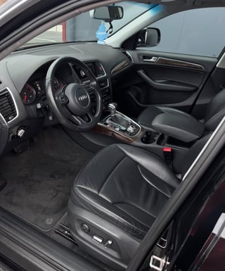 Interior of Audi vehicle showing black leather steering wheel, dashboard, center console, and black leather seats