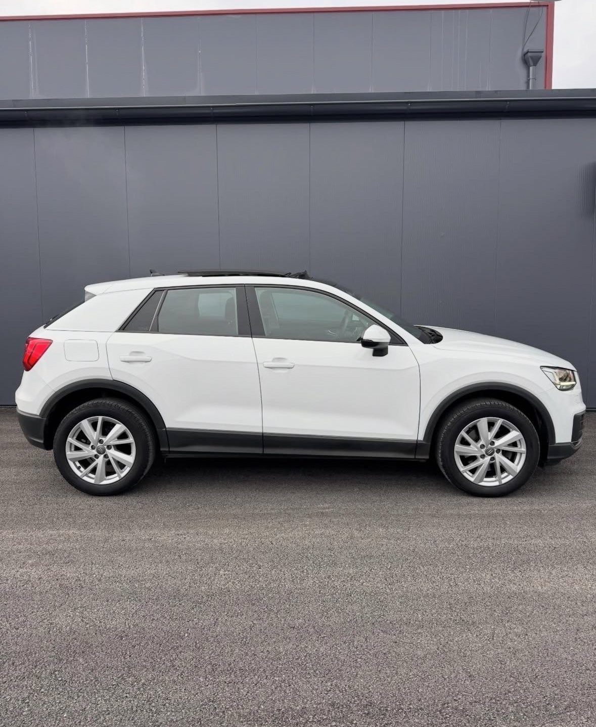 White compact SUV parked in front of a dark gray building with metal siding