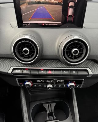 Car dashboard displaying backup camera view with purple parking guidelines overlay and dual round air vents above climate controls