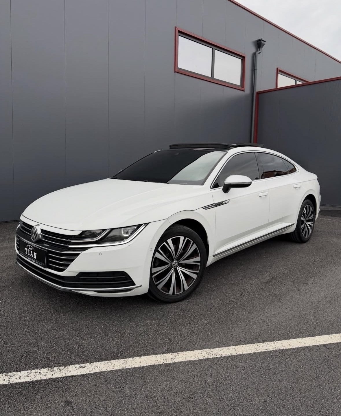 White Volkswagen Arteon luxury sedan parked in front of a gray industrial building with red trim