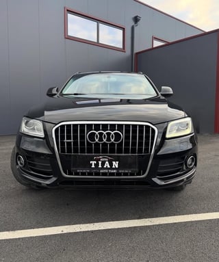 Black Audi sedan with vertical grille parked in front of gray industrial building