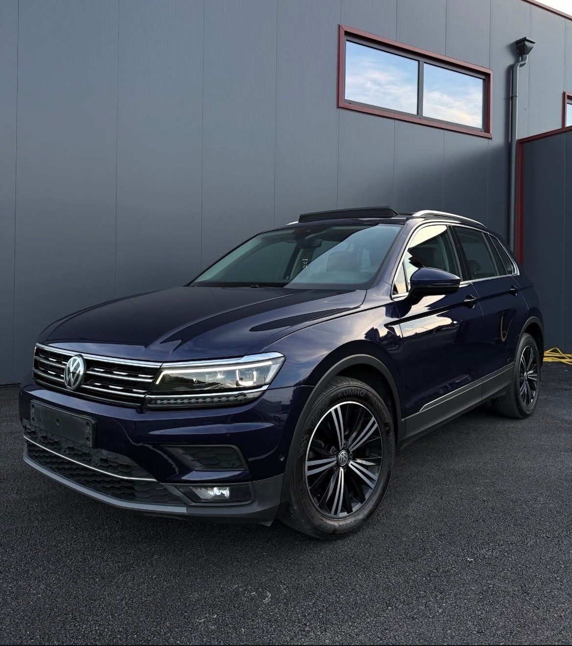 Dark blue Volkswagen SUV parked in front of a gray building with red trim and a window