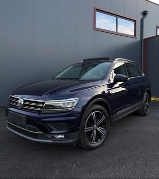 Dark blue Volkswagen SUV parked in front of a gray building with red trim and a window