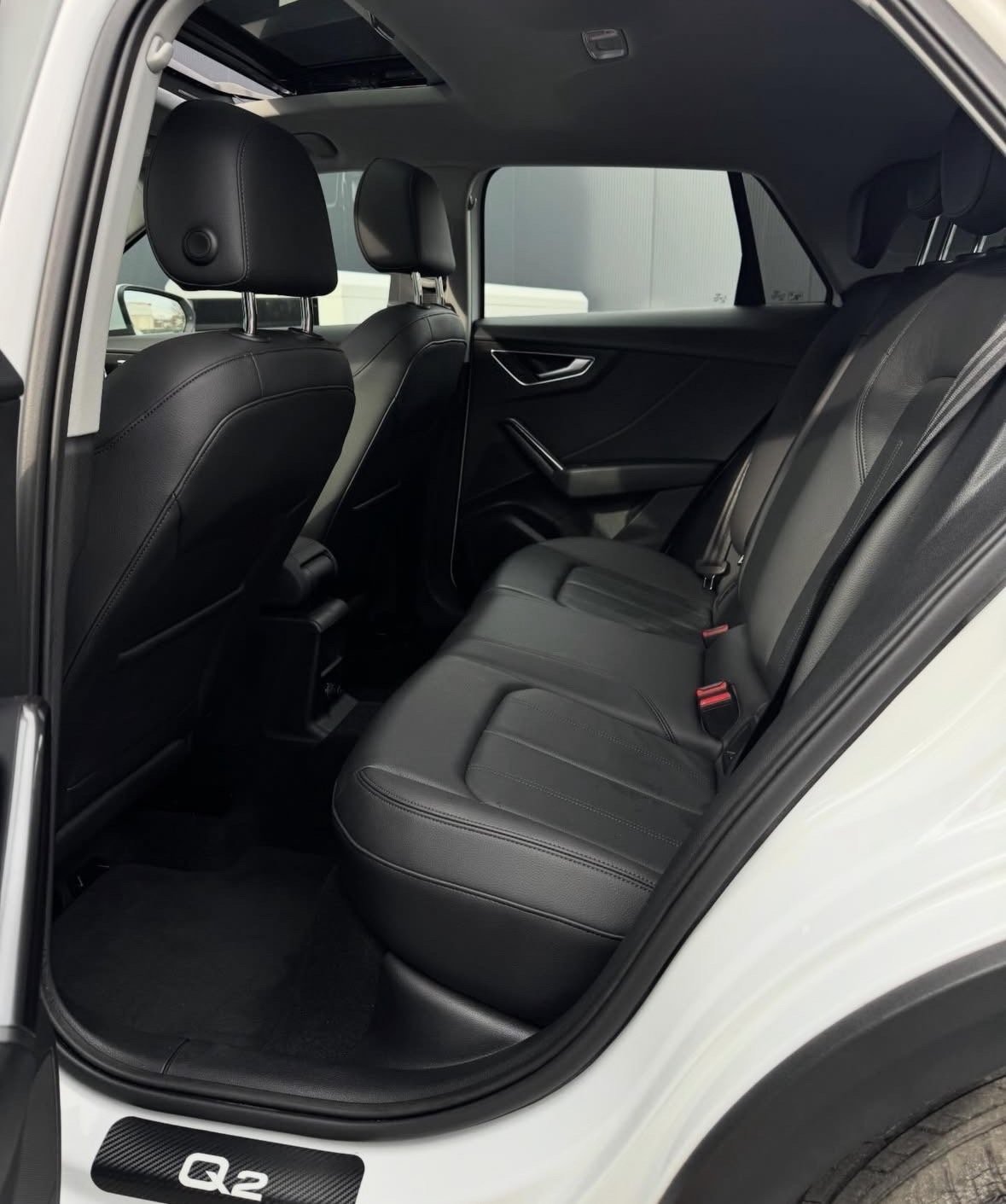 Interior view of a cars back seat with black leather upholstery, showing open rear passenger door and headrests
