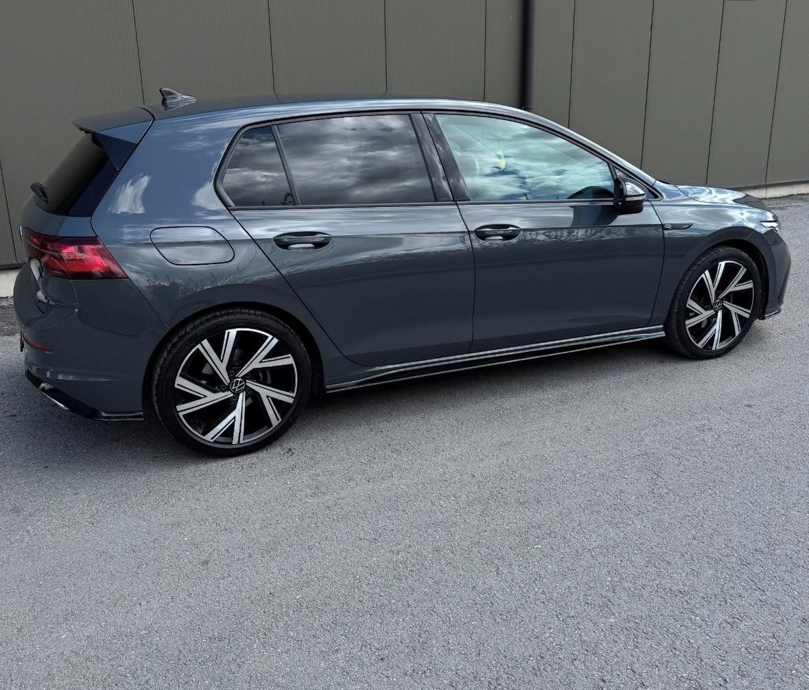 Dark blue Volkswagen Golf hatchback parked on gray asphalt with corrugated metal wall background