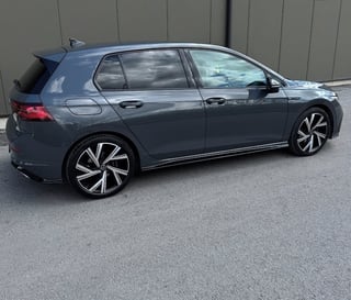 Dark blue Volkswagen Golf hatchback parked on gray asphalt with corrugated metal wall background