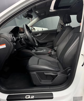 Interior of white Audi Q2 with black leather seats, steering wheel, and dashboard viewed from drivers side door open