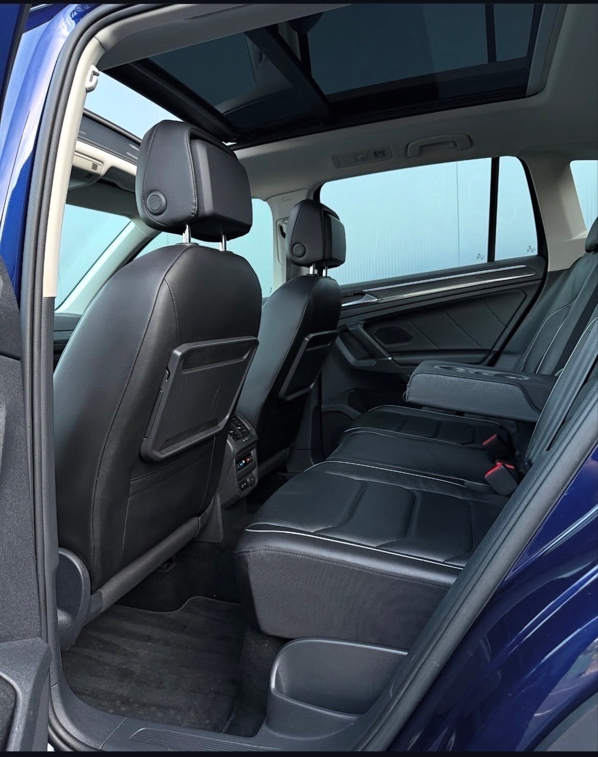 Interior view of a blue SUV showing black leather seats, headrests, panoramic sunroof, and rear passenger seating