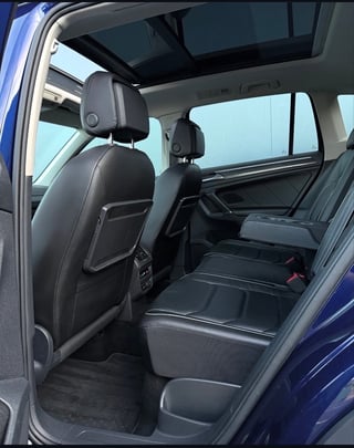 Interior view of a blue SUV showing black leather seats, headrests, panoramic sunroof, and rear passenger seating