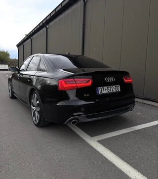 Black Audi A6 sedan parked in a lot next to a dark metal building