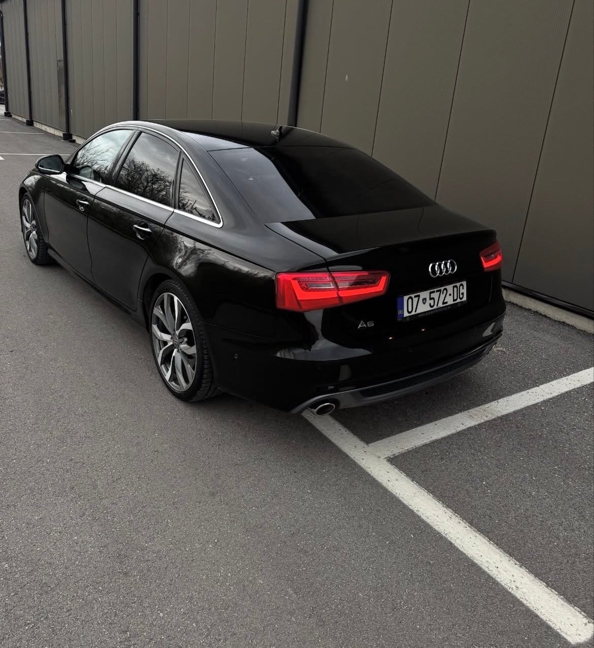 Black Audi A4 sedan parked in a parking space against a corrugated metal wall