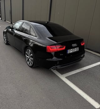 Black Audi A4 sedan parked in a parking space against a corrugated metal wall
