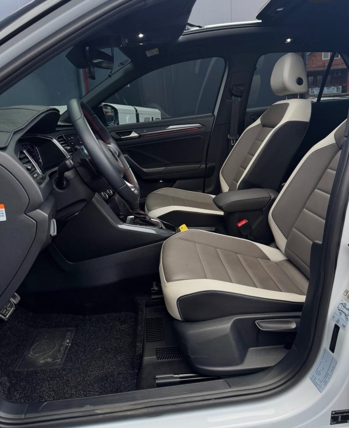 Interior of a white vehicle showing black and beige leather seats with contrast stitching, steering wheel, and open drivers side door