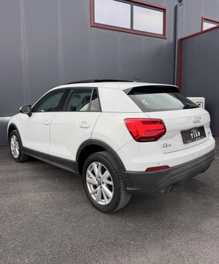 White Audi Q4 compact SUV photographed from the rear three-quarter angle in an industrial garage setting