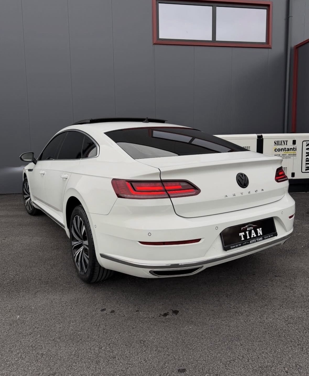 White sedan car parked in garage with red taillights and black license plate visible from rear angle