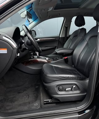 Interior view of a car showing drivers side with black leather seats, steering wheel, and dashboard through open door