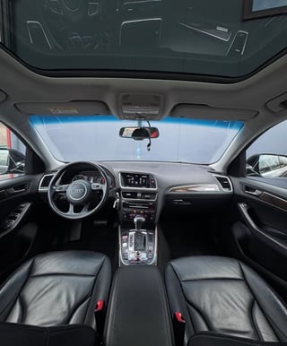 Interior view of an Audi vehicle showing steering wheel, dashboard, black leather seats, and windshield with blue sky visible