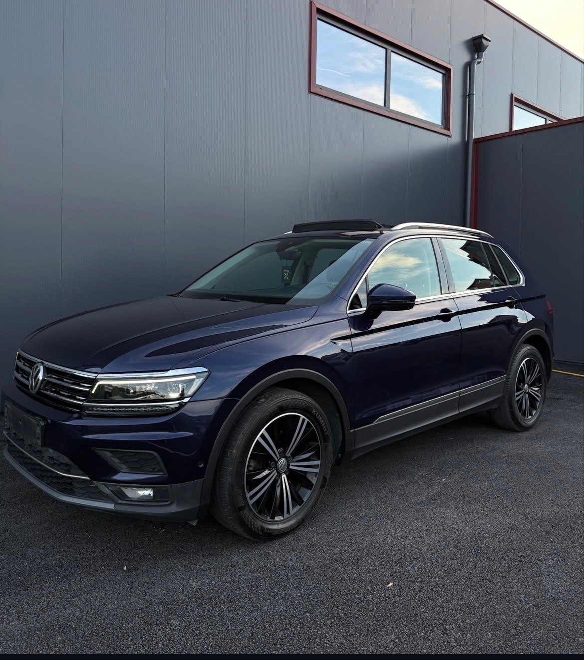 Blue Volkswagen Tiguan SUV parked against a gray industrial building with windows