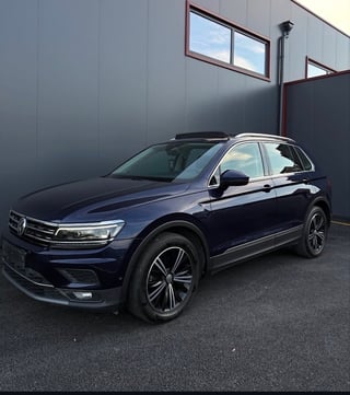 Blue Volkswagen Tiguan SUV parked against a gray industrial building with windows