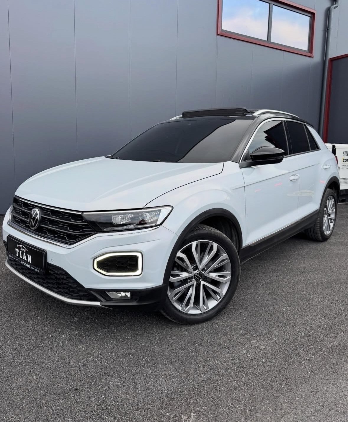 White Volkswagen T-Roc SUV parked in front of a gray industrial building with red window frames