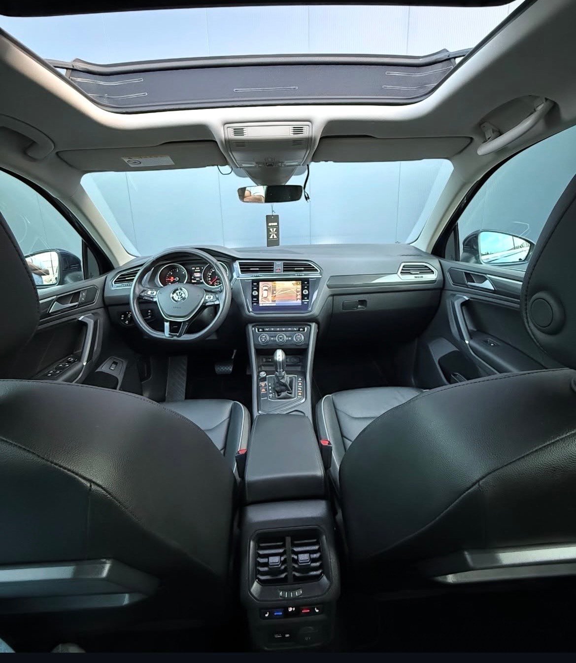 Interior view of a car dashboard and steering wheel with panoramic sunroof, black leather seats, and center touchscreen display