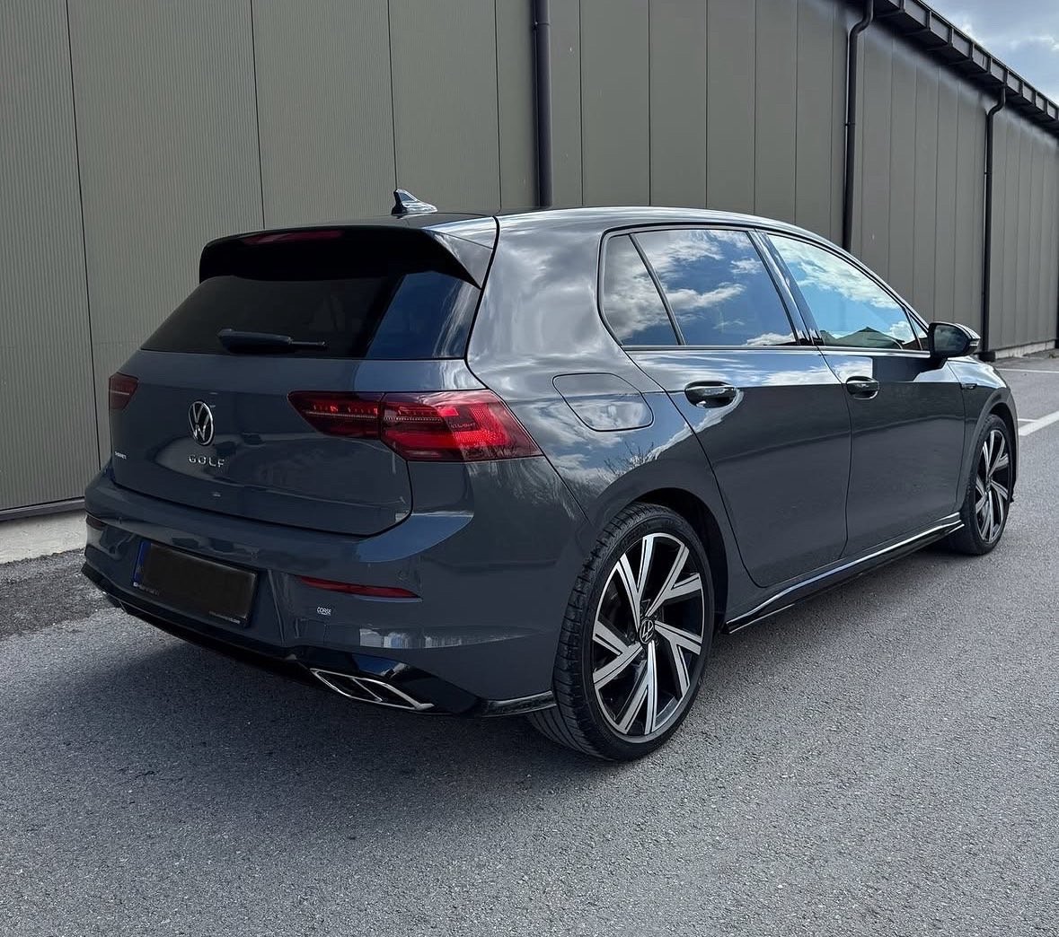 Dark blue Volkswagen Golf hatchback parked against a metal industrial building with gray concrete pavement