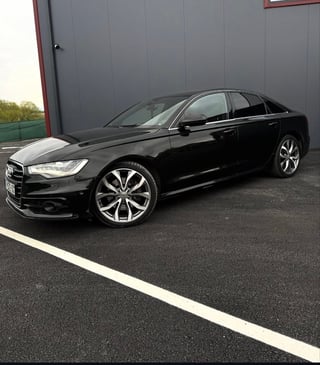 Black luxury sedan parked in front of a gray building with modern alloy wheels and sleek design
