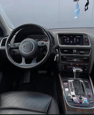 Audi car interior showing black steering wheel, digital dashboard, and gear shift, viewed from driver seat