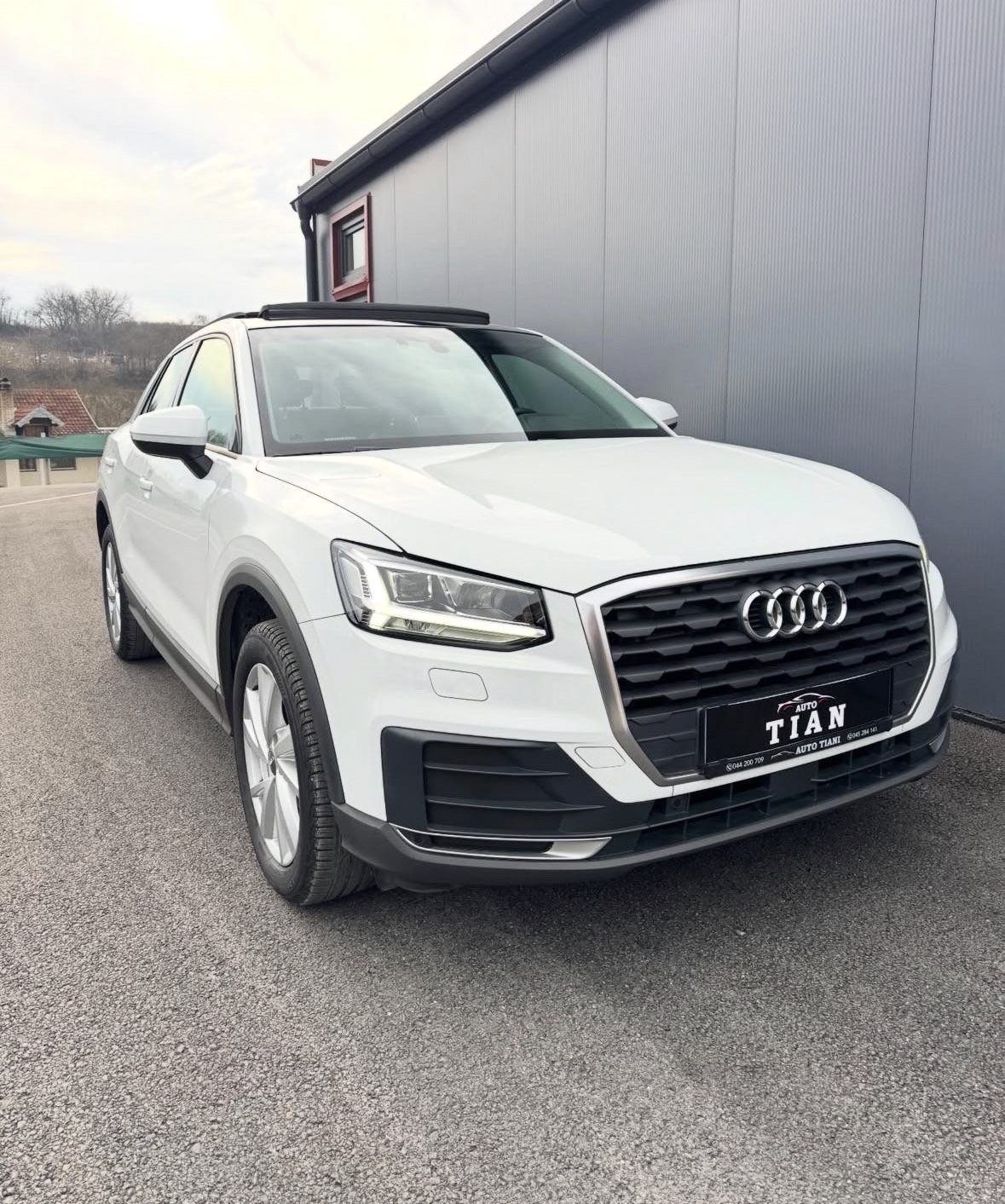 White Audi Q2 SUV parked in front of a gray metal building with dealership signage