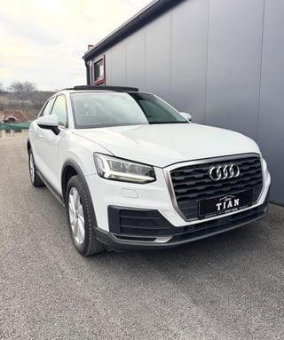 White Audi Q2 SUV parked in front of a gray metal building with dealership signage