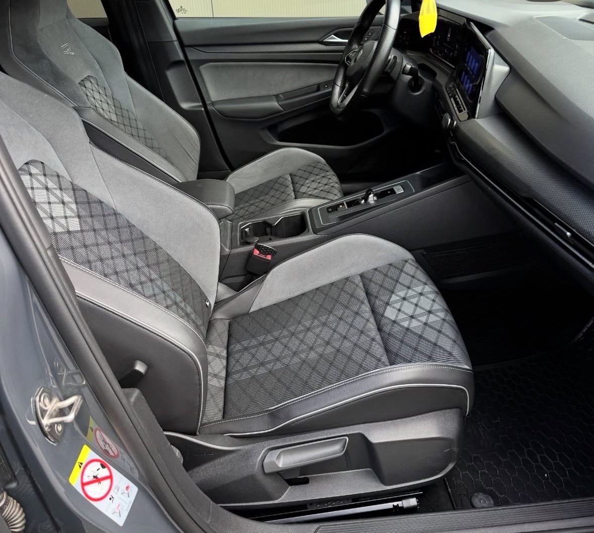 Interior view of a car with gray and black quilted upholstery, steering wheel, dashboard, and manual transmission shifter visible