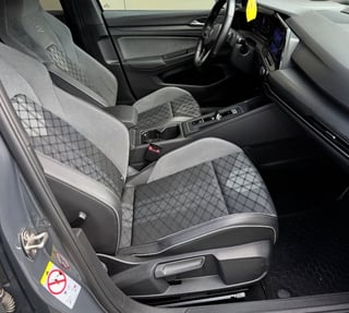 Interior view of a car with gray and black quilted upholstery, steering wheel, dashboard, and manual transmission shifter visible