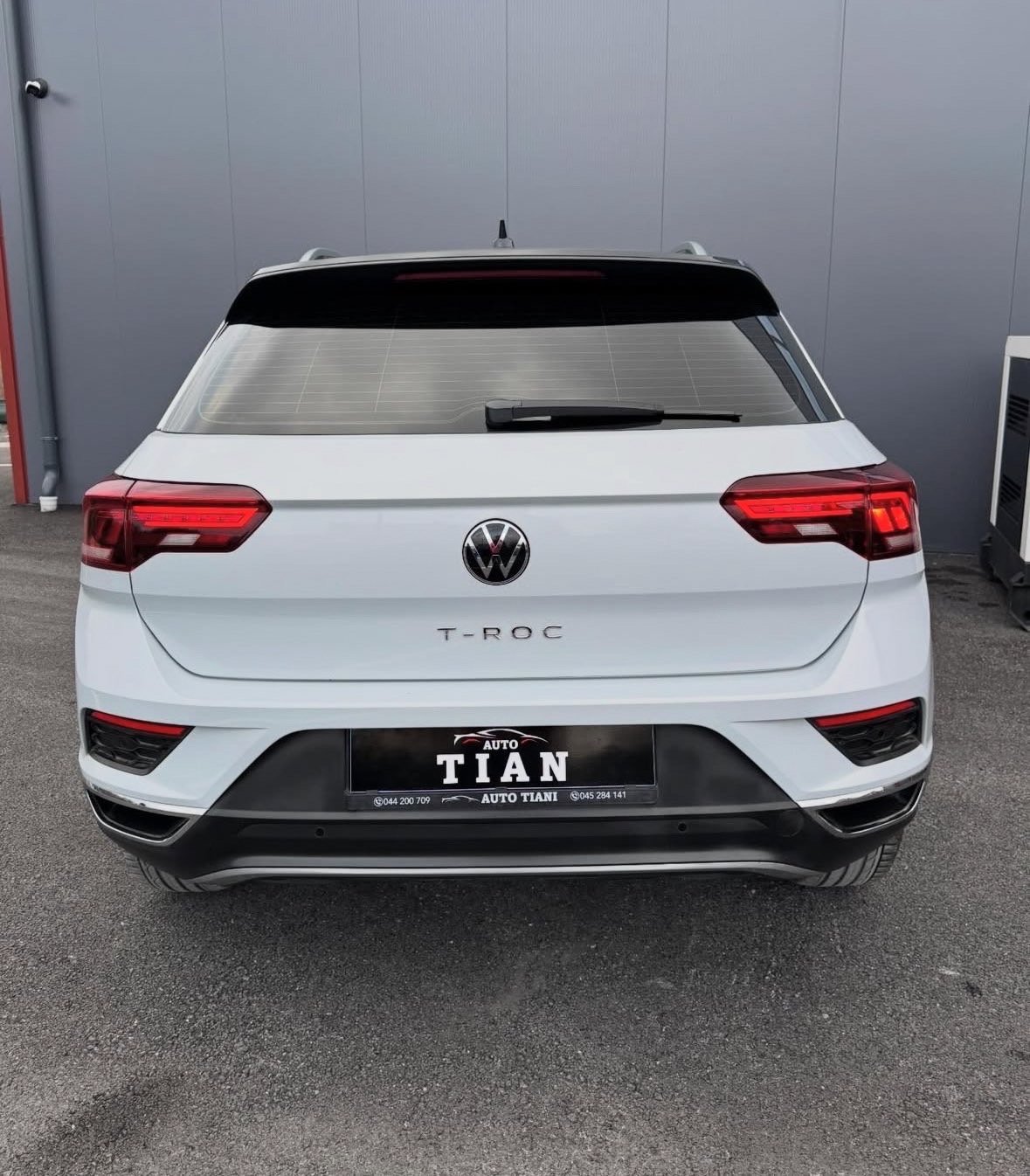 Rear view of a white Volkswagen T-Roc hatchback with red taillights parked in a dealership lot