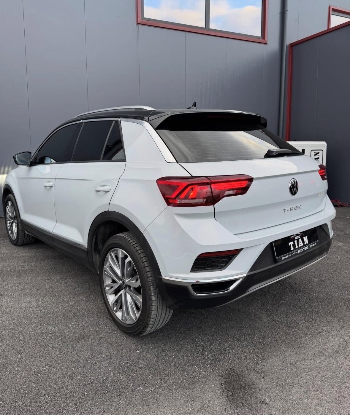 White Volkswagen T-Roc compact SUV parked outdoors, rear three-quarter view showing red taillights and metallic wheels
