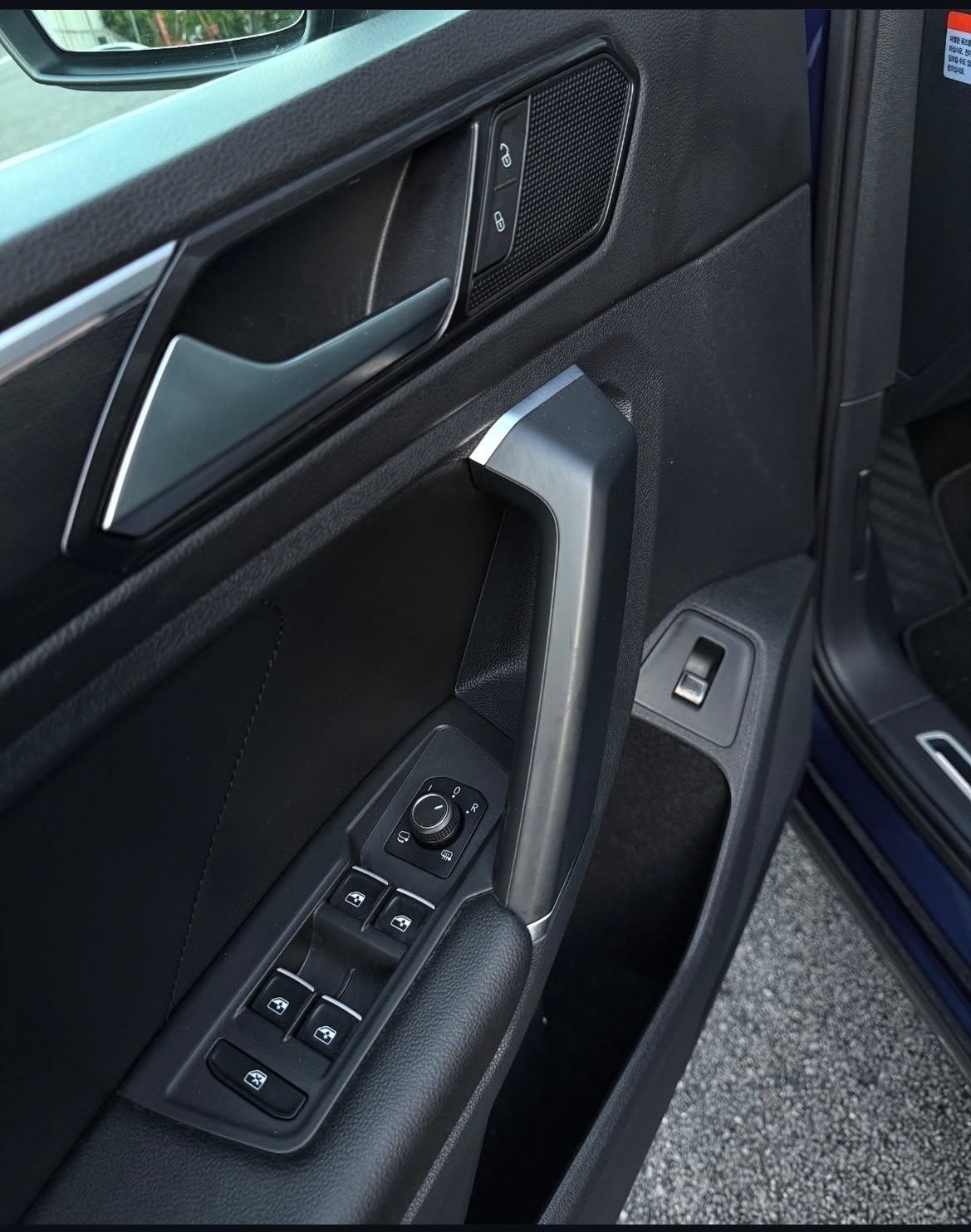 Car door interior panel showing window control buttons, door handle, and speaker grille in dark gray and black